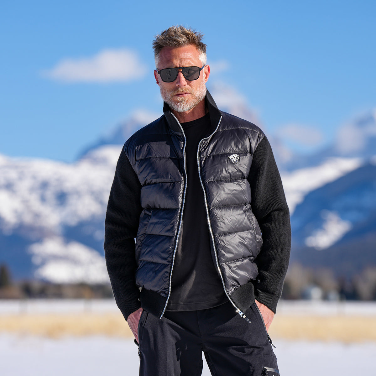 Aspen Knit Puffer in black with knit sleeves, in a snowy field with mountains behind